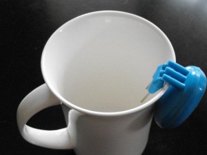 A plastic blue liquid level indicator hooks onto the side edge of a white mug. 