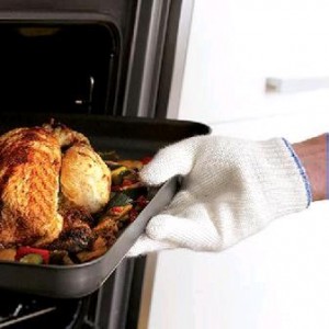 A hand wears a white oven glove. The hand is lifting a tray of roast chicken out of the oven.