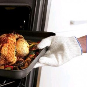 A hand wears a white oven glove. The hand is lifting a tray of roast chicken out of the oven. 